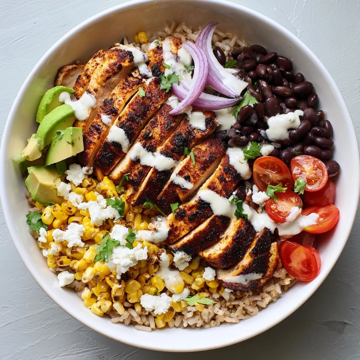 Sliced juicy chicken atop protein packed street corn chicken bowl with fresh cilantro, tomatoes, and crumbled cotija