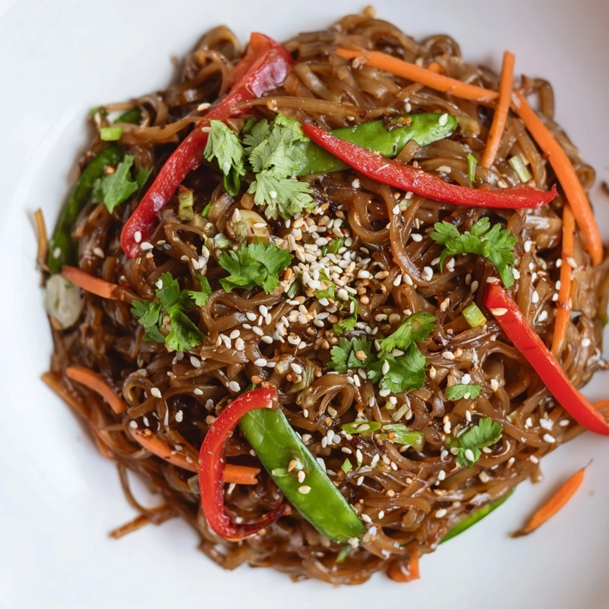 Garnished rice noodle stir fry plated with fresh cilantro and sesame seeds