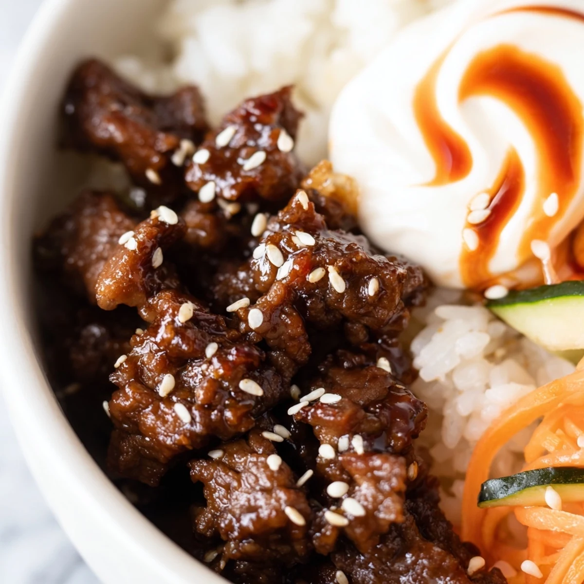 Golden Korean beef bowl with spicy mayo drizzle served over fluffy white rice alongside crisp colorful vegetables