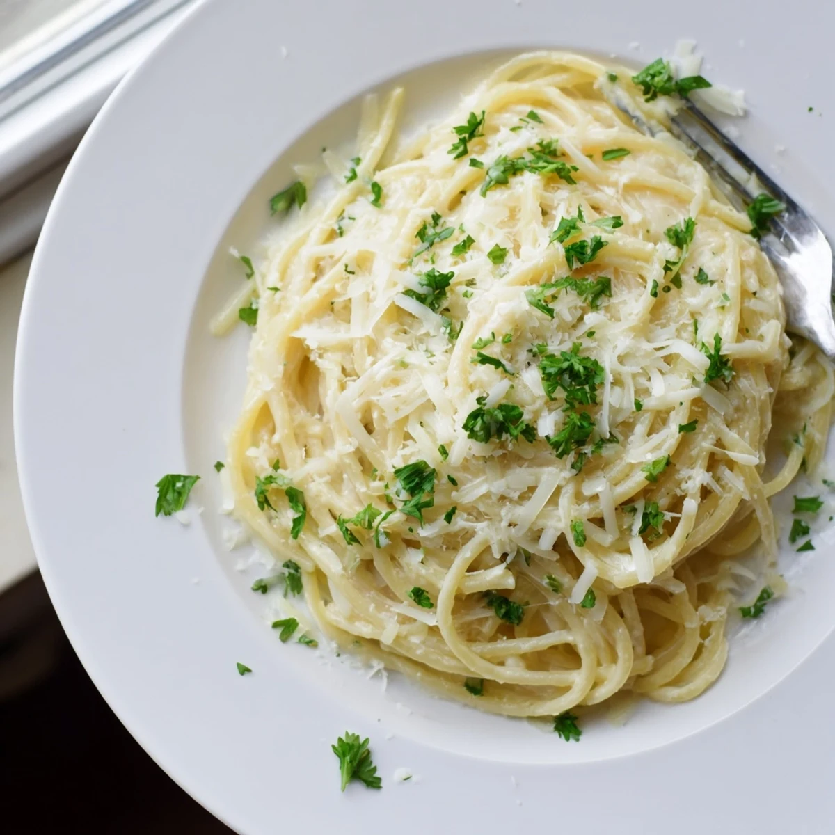 Creamy parmesan cheese sauce clings to al dente garlic butter spaghetti noodles in a close-up view.