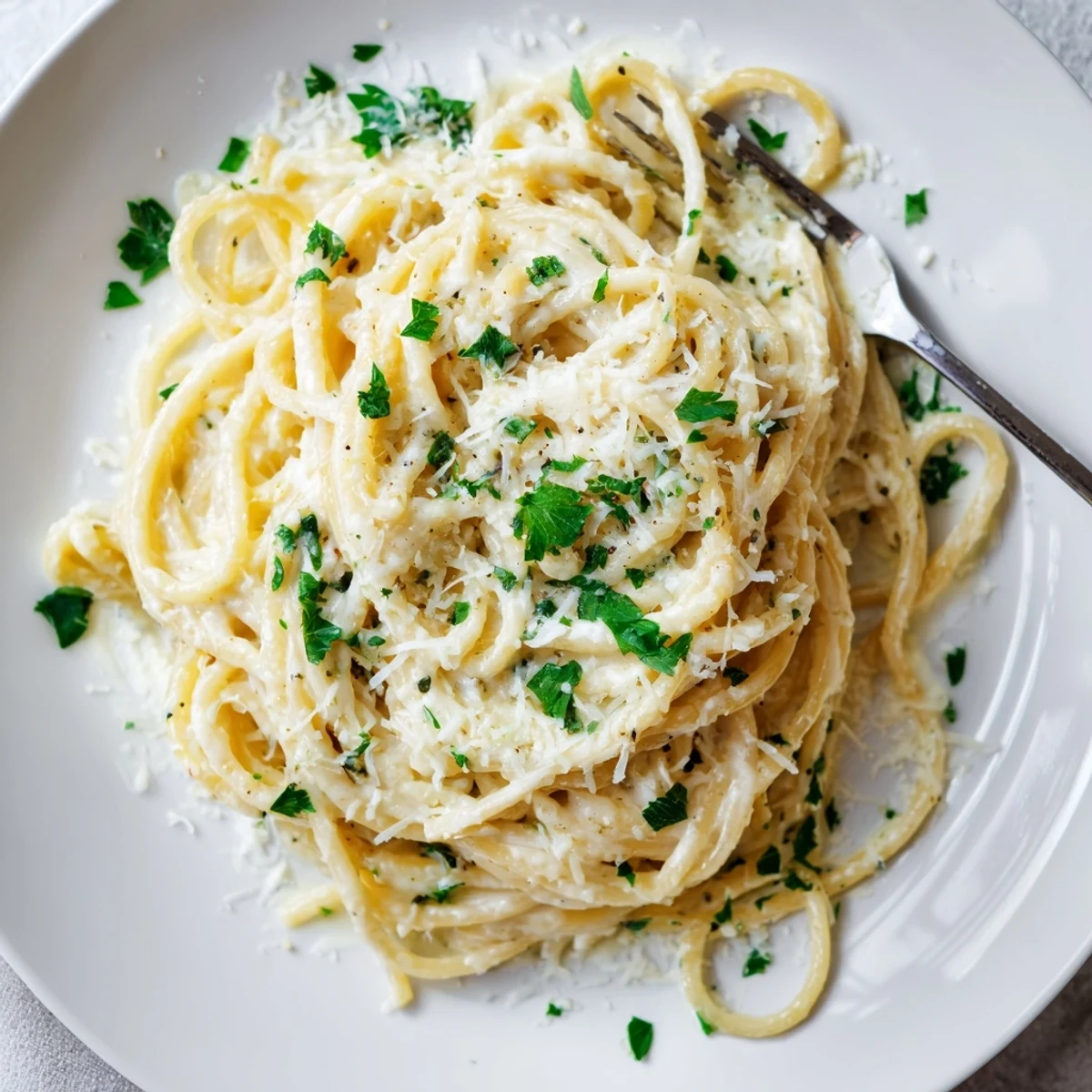 Plate of steaming cheesy garlic parmesan spaghetti topped with extra grated cheese and parsley.