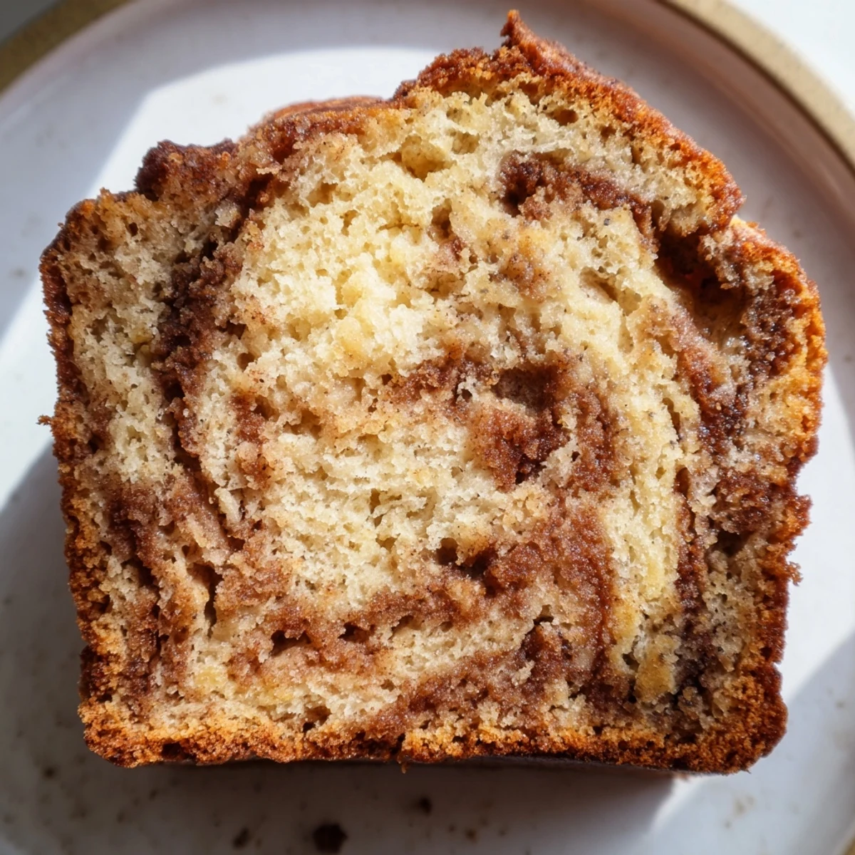 Warm Cinnamon Sugar Swirl Banana Bread loaf topped with crunchy sweet cinnamon crust on rustic wooden board