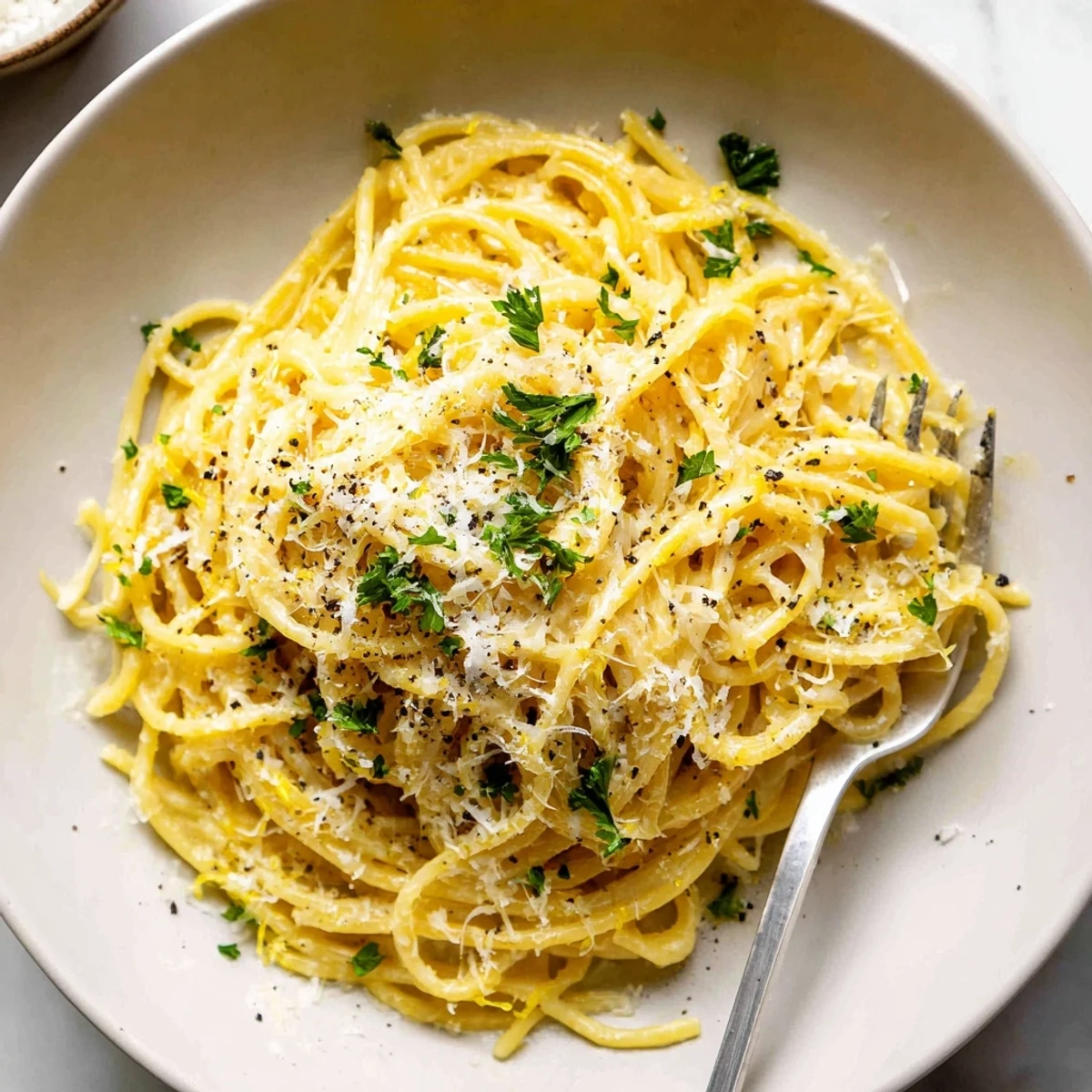 Creamy Parmesan lemon pasta twirled in a skillet with fresh herbs and black pepper