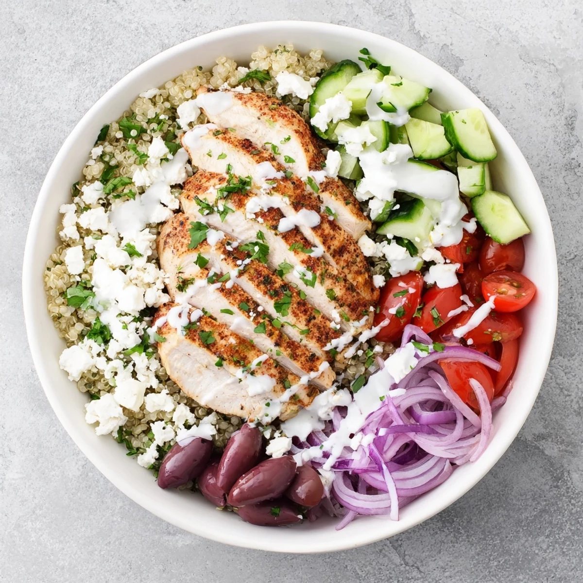 Golden Mediterranean chicken quinoa bowl topped with fresh cucumbers, tomatoes, and crumbled feta cheese