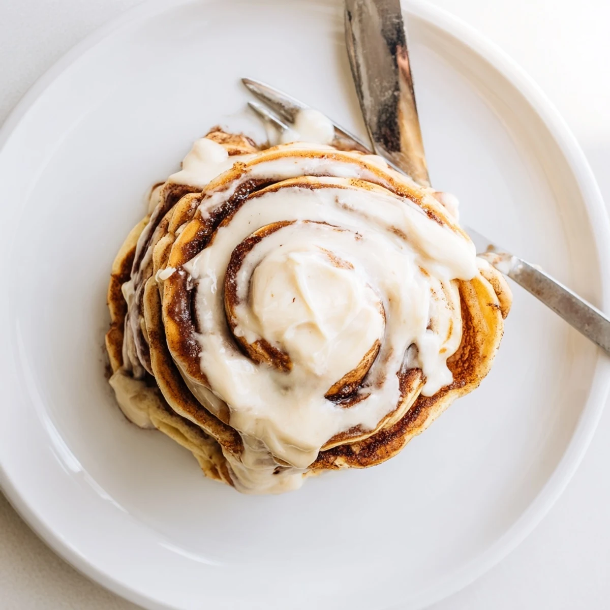 Golden cinnamon roll pancakes drizzled with creamy icing on a white plate