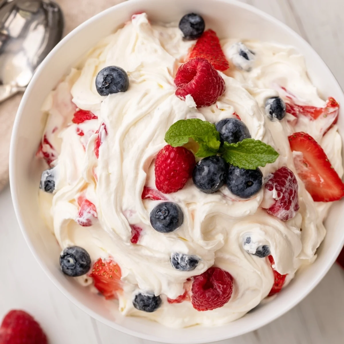 Red White Blue Cheesecake Salad piled in bowl, creamy berries and mint  