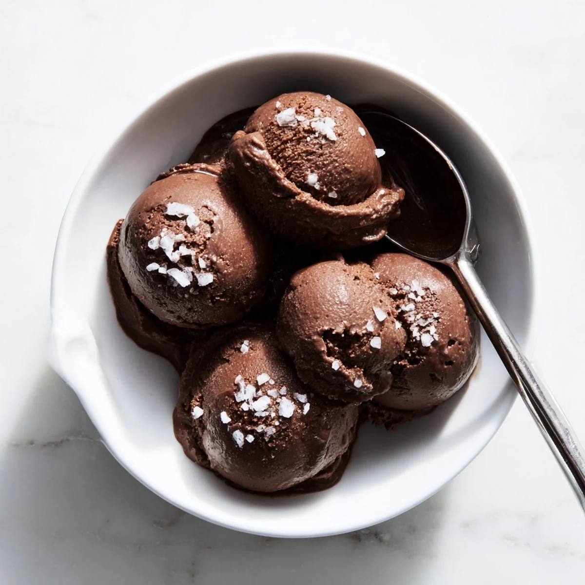 Homemade chocolate sourdough ice cream garnished with flaky sea salt and served in a porcelain dessert bowl