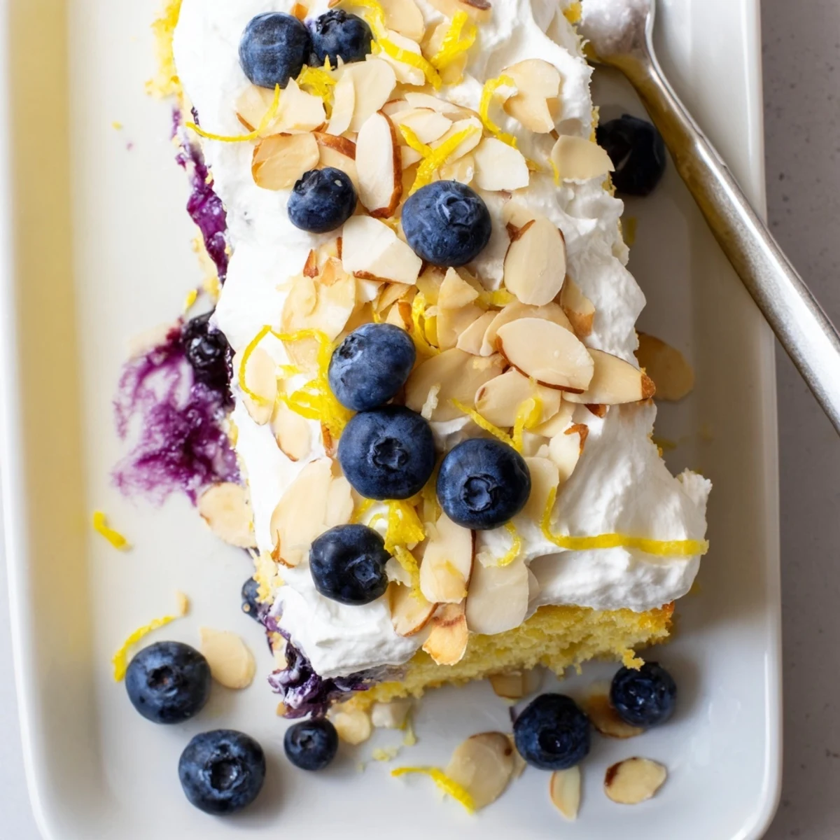Golden lemon blueberry poke cake topped with fluffy whipped cream and toasted sliced almonds