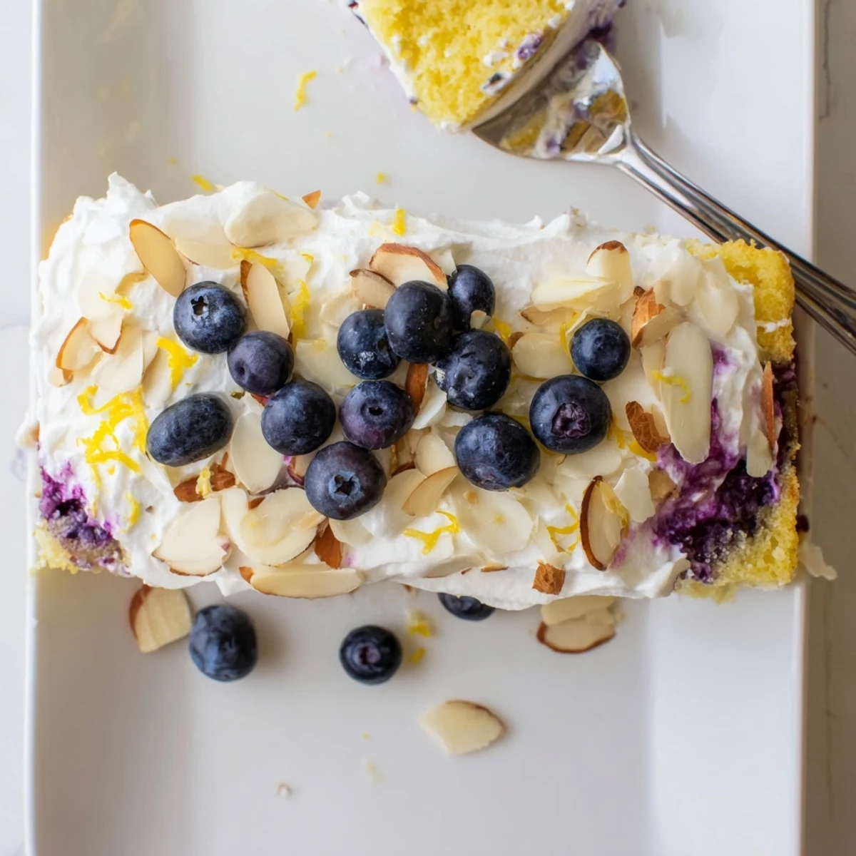 Slice of lemon blueberry poke cake showing syrup-soaked layers with whipped cream and almonds