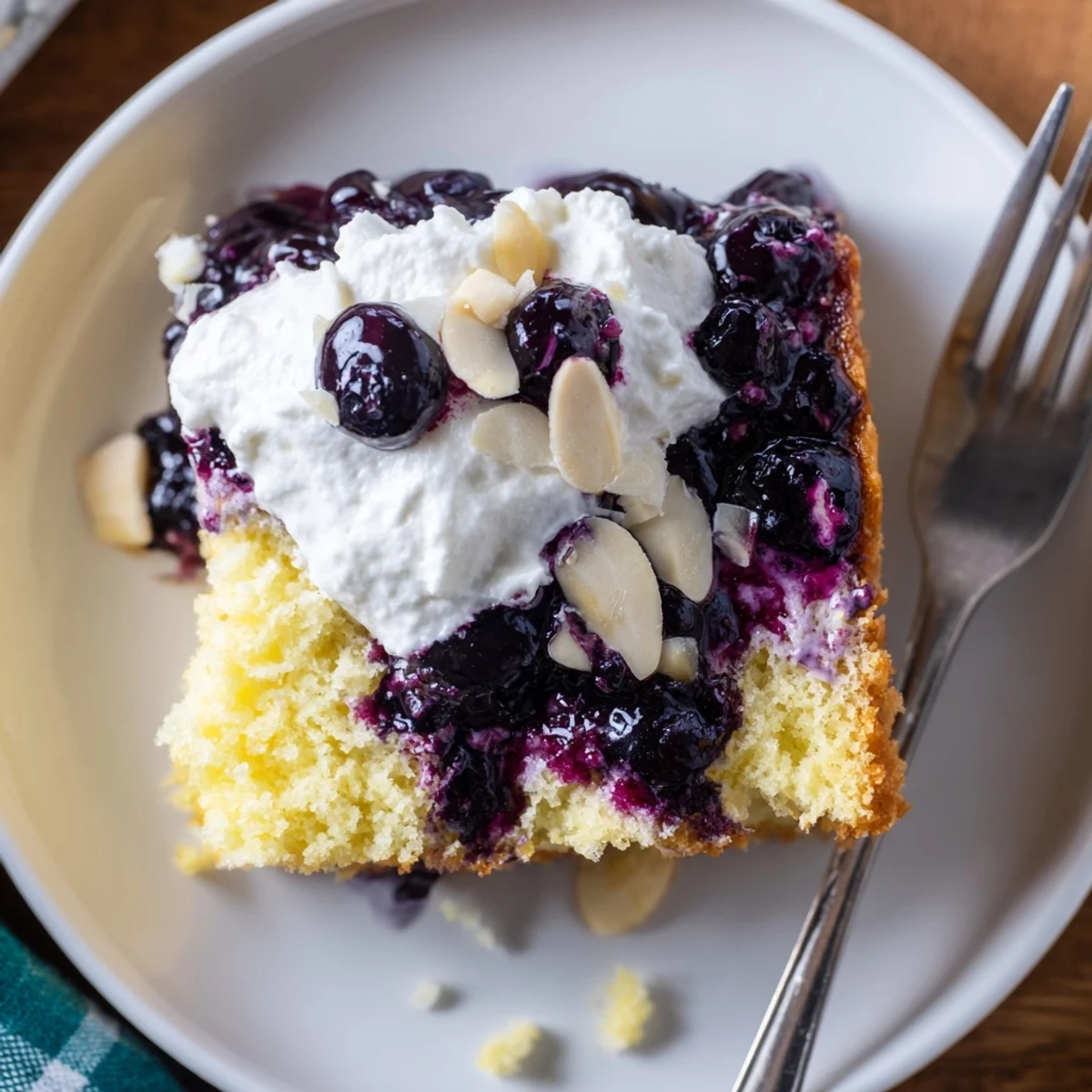Warm lemon blueberry sauce soaking into Lemon Blueberry Poke Cake With Almond Topping