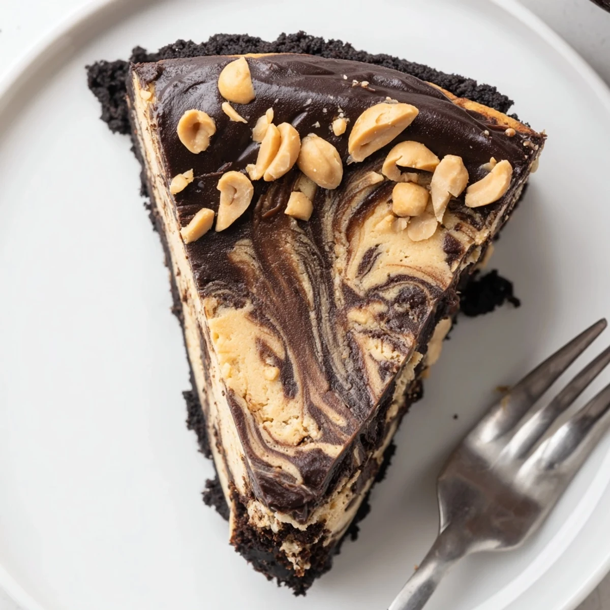 Chocolate peanut butter cheesecake sliced thick topped with glossy ganache and chopped peanuts